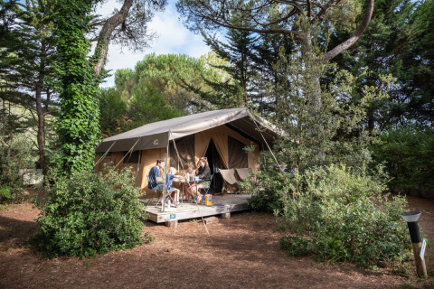 Familia disfruta de una comida frente a la tienda safari Toile&Bois tent Sweet rodeada de árboles.
