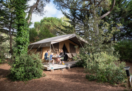 Famille prenant un repas devant une tente safari Toile&Bois tent Sweet dans un cadre boisé.
