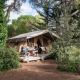 Familie sidder ved et bord foran en safari-telt Toile&Bois tent Sweet i grønne omgivelser.