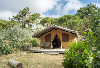 Safari teltet Toile&Bois ved Huttopia Chardons Bleus - Ile de Ré, omgivet af grønne træer og buske.
