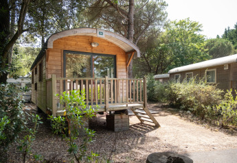 Houten hut Roulotte omgeven door bomen bij Huttopia Chardons Bleus - Ile de Ré, Frankrijk, in de zon.
