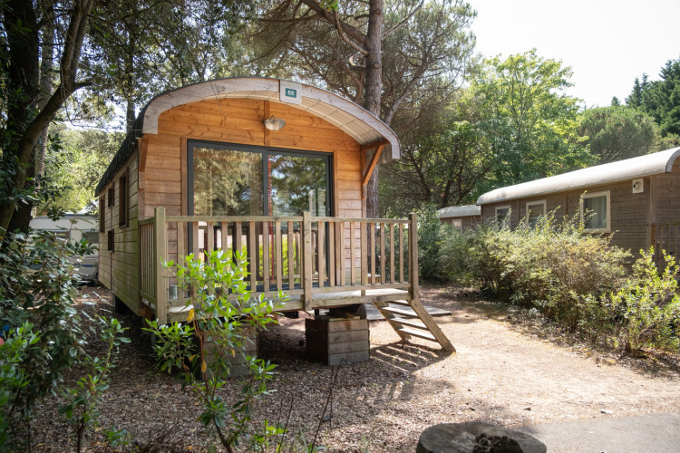 Cabaña de madera Roulotte entre árboles en Huttopia Chardons Bleus - Ile de Ré, Francia, en un día soleado.