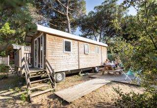 Una familia disfruta de una comida al aire libre junto a una cabaña de madera en Huttopia Chardons Bleus, Ile de Ré.