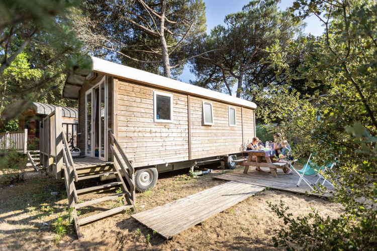 Una familia disfruta de una comida al aire libre junto a una cabaña de madera en Huttopia Chardons Bleus, Ile de Ré.