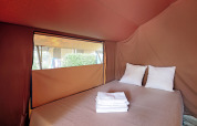 Interior of Bungalow tent Classic at Huttopia Vallouise, with double bed, linen, and a view outside.