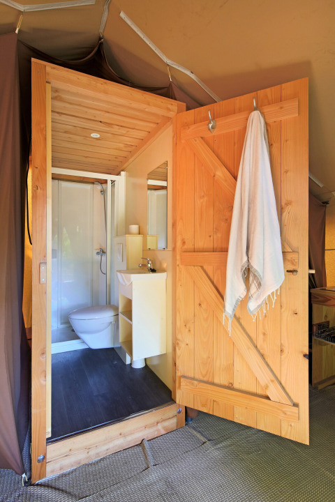 Baño moderno con puerta de madera, toalla, inodoro y ducha dentro de una lujosa tienda safari.