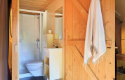 Modern bathroom with a wooden door, towel, toilet, and shower inside a luxury safari tent setup.