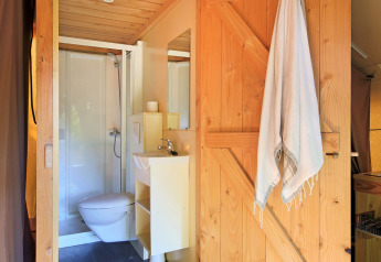 Salle de bain moderne avec porte en bois, serviette, toilettes et douche dans une tente safari de luxe.