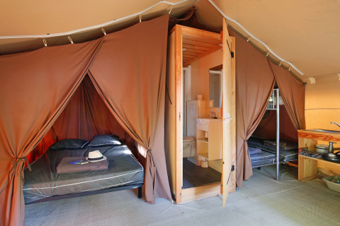 Innenansicht eines Safarizelts mit Doppelbett, Etagenbett, eigenem Bad und kleiner Küchenzeile.