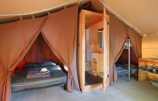 Interior de una tienda safari con cama doble, litera, baño privado y pequeña zona de cocina equipada.