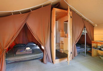 Indvendigt billede af et safaritelts soveværelse, badeværelse og lille køkken, med dobbelt- og enkeltsenge.
