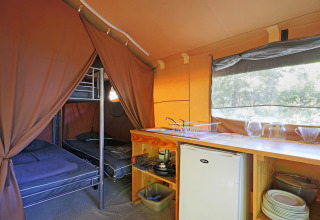Binnenkant van een Toile & bois Sweet safaritent met stapelbedden en kitchenette in Huttopia Beaulieu sur Dordogne.