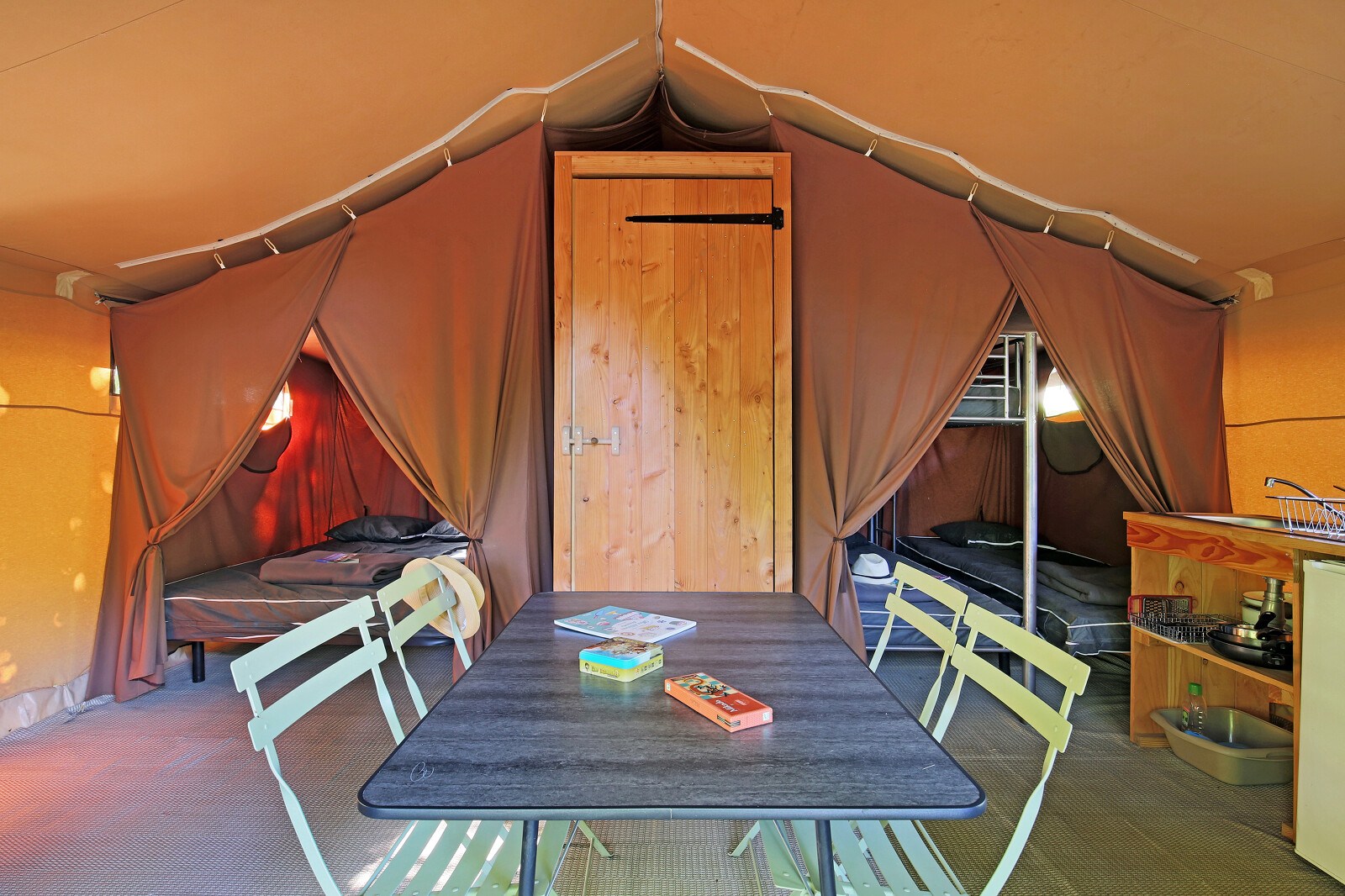 Interieur van een safaritent met eettafel, twee slaapruimtes, stapelbed en klein keukentje.