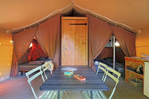 Interior de una tienda safari con mesa de comedor, dos zonas de cama, literas y una pequeña cocina.