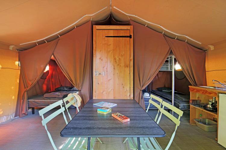 Interior of a safari tent with dining table, two sleeping areas, bunk beds, and a small kitchenette.
