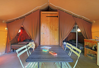 Intérieur d'une tente safari avec table à manger, deux coins couchage, lits superposés et kitchenette.