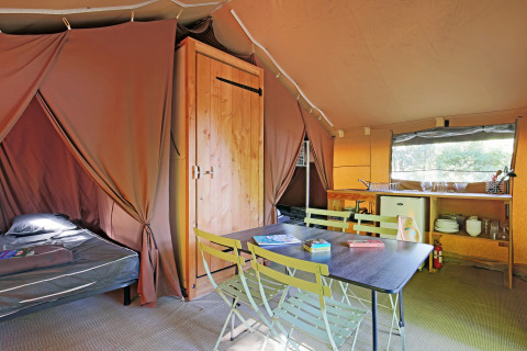 Vista interior de una tienda safari en Huttopia Beaulieu sur Dordogne con mesa, cama y zona de cocina.