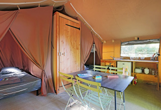Vista interior de una tienda safari en Huttopia Beaulieu sur Dordogne con mesa, cama y zona de cocina.