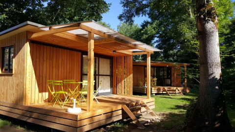 Udsigt til Chalet Evasion træhytte med gul terrasse og havemøbler midt i en grøn, skovklædt natur.
