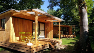 Udsigt til Chalet Evasion træhytte med gul terrasse og havemøbler midt i en grøn, skovklædt natur.