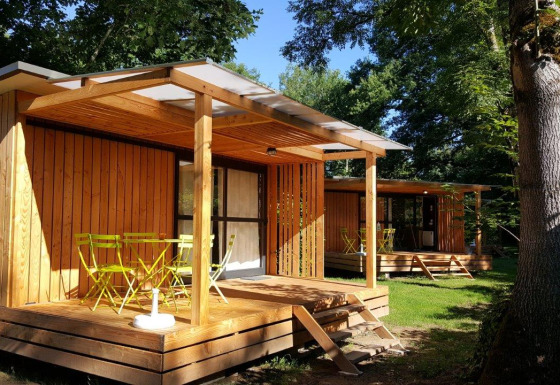 Udsigt til Chalet Evasion træhytte med gul terrasse og havemøbler midt i en grøn, skovklædt natur.