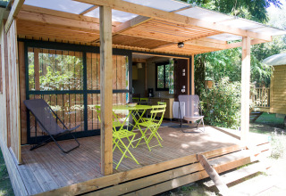Træhytte med overdækket terrasse og havemøbler ved Chalet Evasion, Huttopia Beaulieu sur Dordogne, Frankrig.