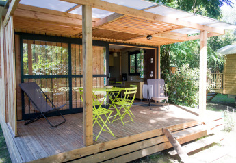 Træhytte med overdækket terrasse og havemøbler ved Chalet Evasion, Huttopia Beaulieu sur Dordogne, Frankrig.