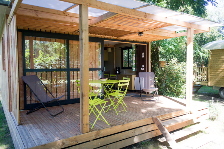 Holzhütte mit überdachter Terrasse und Gartenmöbeln bei Chalet Evasion, Huttopia Beaulieu sur Dordogne, Frankreich.