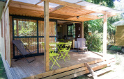 Træhytte med overdækket terrasse og havemøbler ved Chalet Evasion, Huttopia Beaulieu sur Dordogne, Frankrig.
