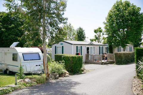 Camping Seasonova Saint Michel in Normandy, France, featuring mobile homes, a caravan, and lush greenery.