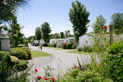 Urlauber gehen einen Pfad entlang von Mobilheimen im Camping Seasonova Saint Michel, Normandie, Frankreich.