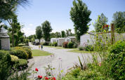 Feriehytter omgivet af grønne planter og blomster på Camping Seasonova Saint Michel i Normandiet, Frankrig.
