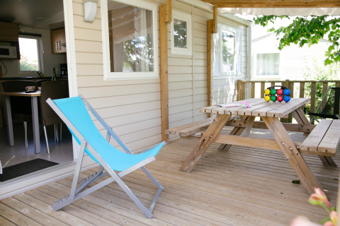 Terraza de madera con silla azul y mesa de picnic en una casa móvil en Camping Seasonova Saint Michel, Normandía, Francia.