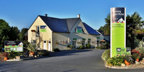 Entrance to Camping Saint Michel holiday park in Normandy, France, showing buildings and lush landscaping.
