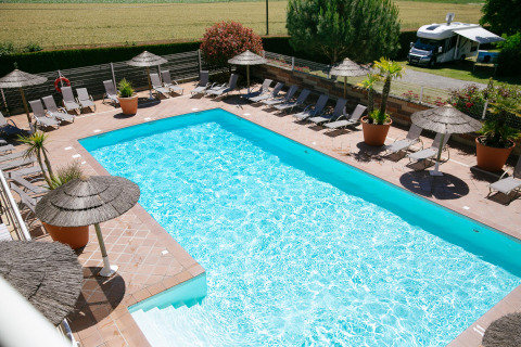 Piscina all’aperto con lettini e ombrelloni al Camping Seasonova Saint Michel in Normandia, Francia.