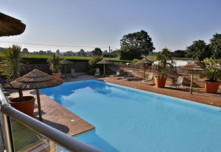 Outdoor swimming pool with loungers and straw umbrellas at Camping Seasonova Saint Michel in Normandy, France.