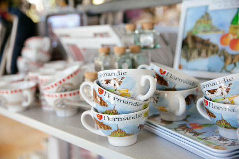 Souvenir mugs from Normandy decorated with colorful local images, displayed at Camping Seasonova Saint Michel.