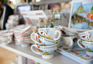 Tasses souvenirs de la Normandie décorées, exposées dans une boutique au Camping Seasonova Saint Michel en France.