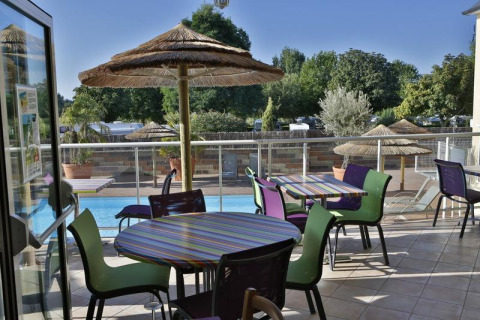 Zona exterior con mesas y piscina en Camping Seasonova Saint Michel, Normandía, Francia, con sombrillas de paja.