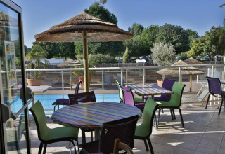 Buitenzitruimte met zicht op zwembad bij Camping Seasonova Saint Michel in Normandië, Frankrijk, met rieten parasols.