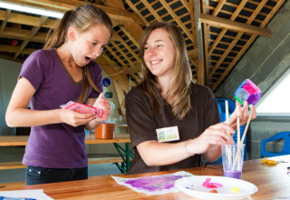 To glade unge kvinder laver farverige kunstprojekter sammen i et opholdsrum på Camping Seasonova Saint Michel.