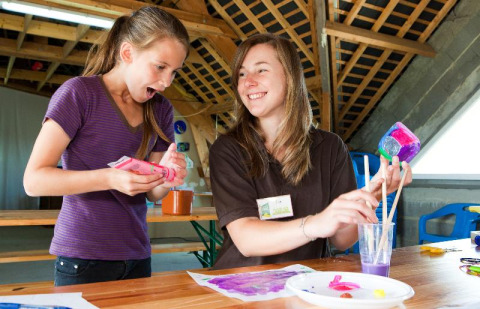 To glade unge kvinder laver farverige kunstprojekter sammen i et opholdsrum på Camping Seasonova Saint Michel.