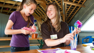 Dos mujeres jóvenes disfrutan de manualidades coloridas en Camping Seasonova Saint Michel en Normandía, Francia.