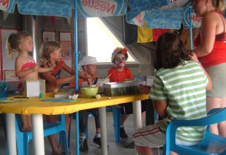 Kinderen doen knutselwerkjes onder parasols aan een tafel bij Camping Seasonova Saint Michel, Normandië, Frankrijk.