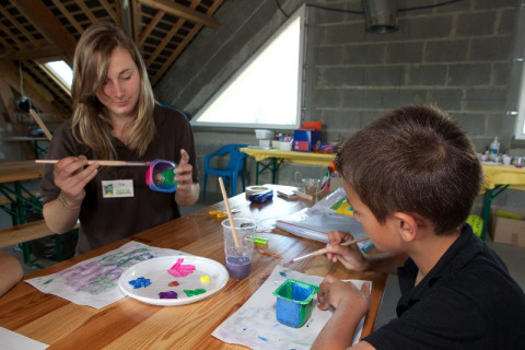 Mujer y niño pintando juntos en una mesa de madera en Camping Seasonova Saint Michel en Normandía, Francia.