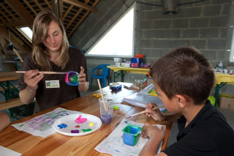 Vrouw en jongen verven samen aan een houten tafel op Camping Seasonova Saint Michel in Normandië, Frankrijk.