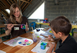 Mujer y niño pintando juntos en una mesa de madera en Camping Seasonova Saint Michel en Normandía, Francia.