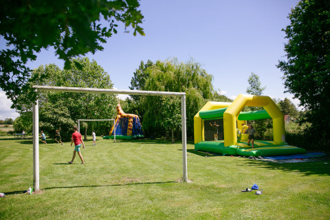 Children play football and enjoy a bouncy castle on the green grounds of Camping Seasonova Saint Michel, France.