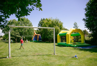 Children play football and enjoy a bouncy castle on the green grounds of Camping Seasonova Saint Michel, France.