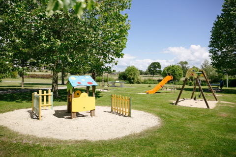 Playground with swings, slide, and playhouse in a green park at Camping Seasonova Saint Michel in Normandy.